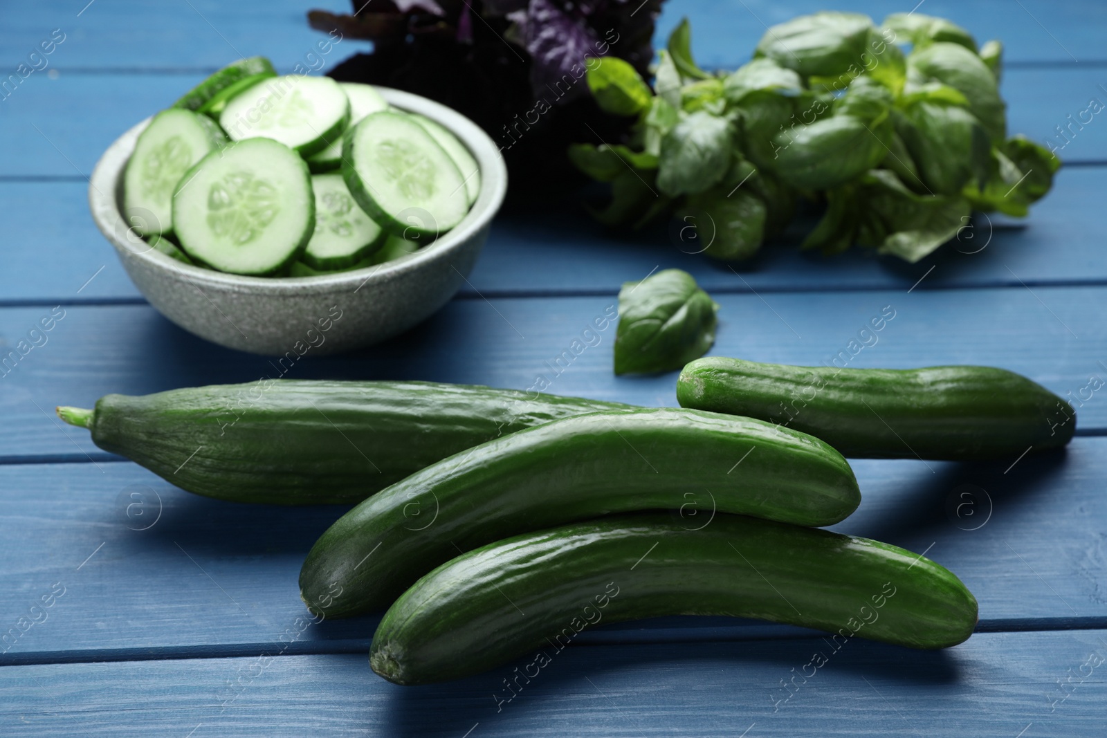 Photo of Fresh ripe cucumbers and greens on blue wooden table