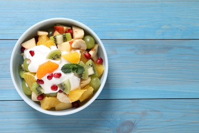 Photo of Delicious fruit salad on light blue wooden table, top view. Space for text