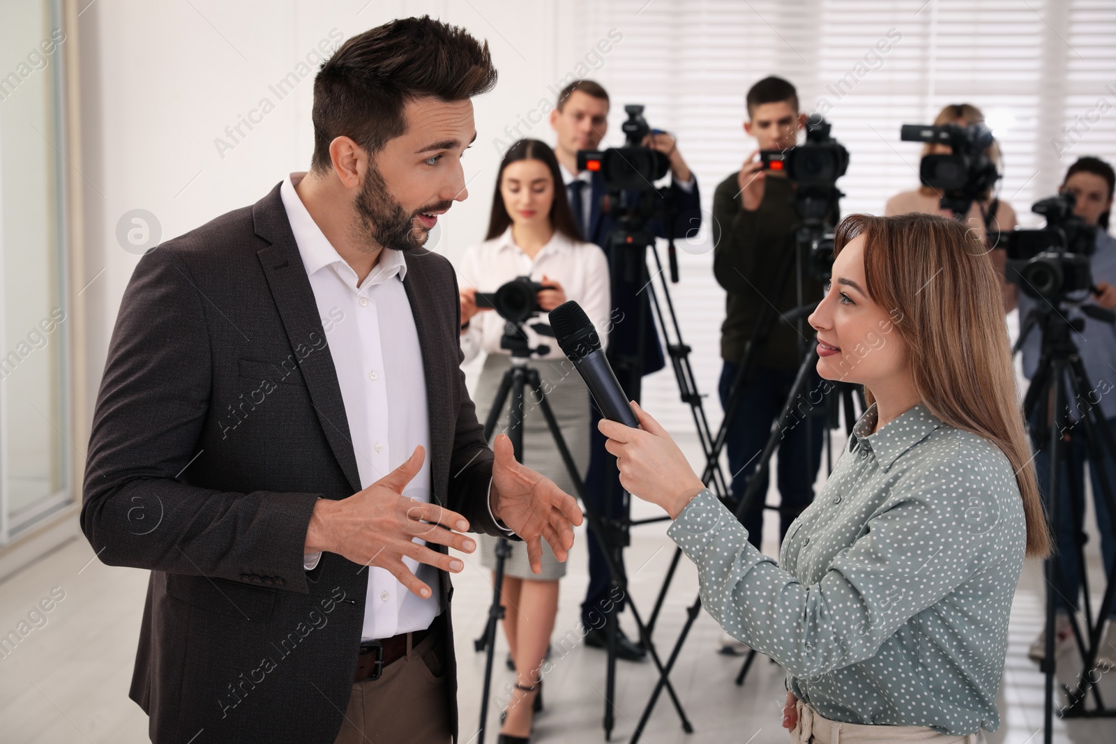 Photo of Professional young journalist interviewing businessman and group of video camera operators on background