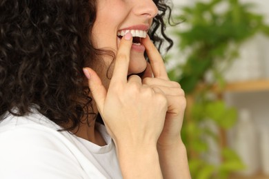 Photo of Young woman applying whitening strip on her teeth indoors, closeup. Space for text
