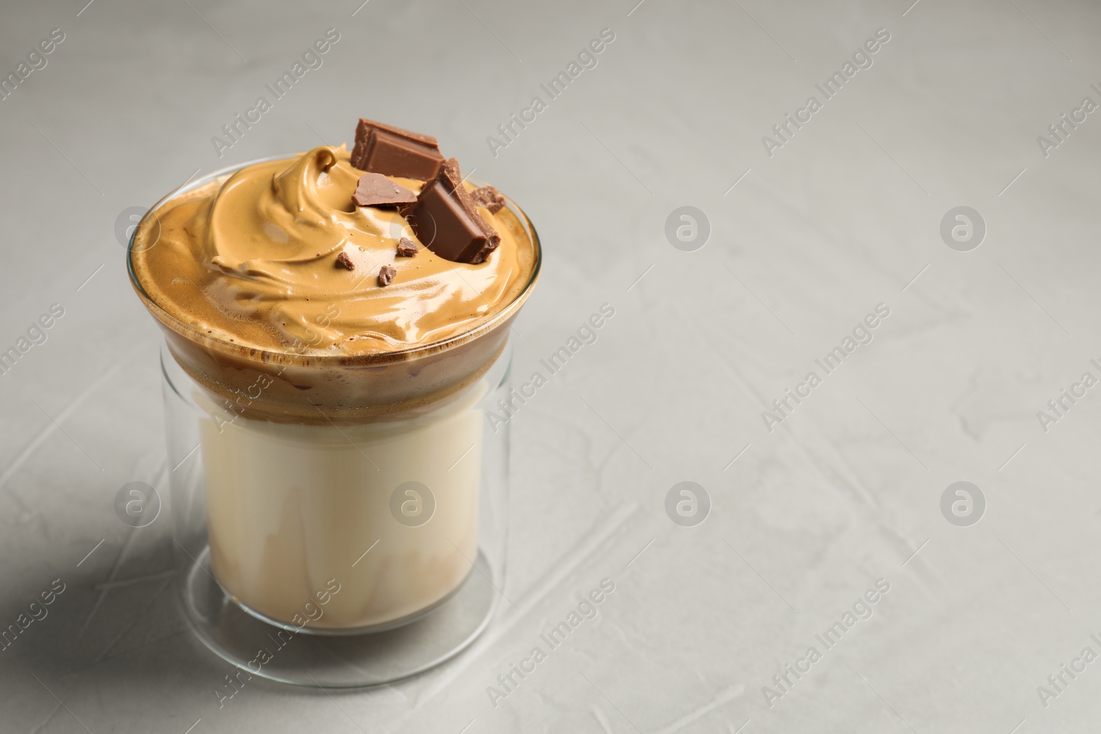 Photo of Glass of delicious dalgona coffee with chocolate on light grey table, space for text