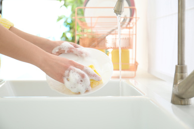 Woman washing ceramic plate in kitchen, closeup