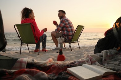 Couple resting near sea at sunset, view from camping tent