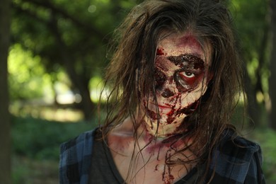 Photo of Scary zombie with bloody face outdoors, closeup. Halloween monster