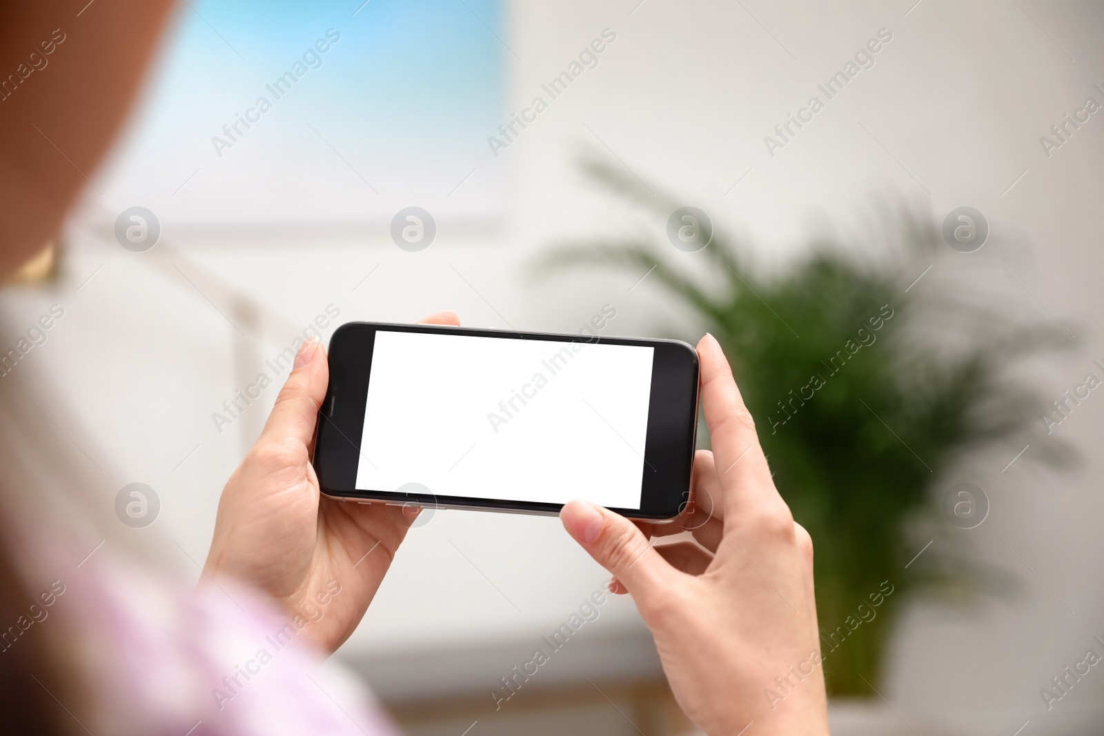 Photo of Woman holding smartphone with blank screen indoors, closeup of hands. Space for text