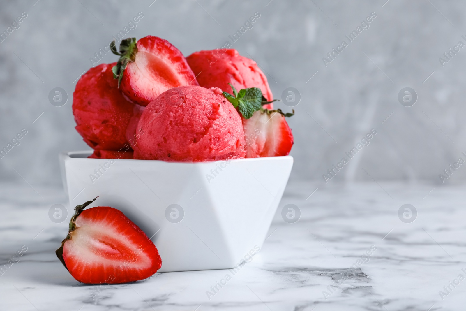 Photo of Yummy strawberry ice cream in bowl on white marble table. Space for text
