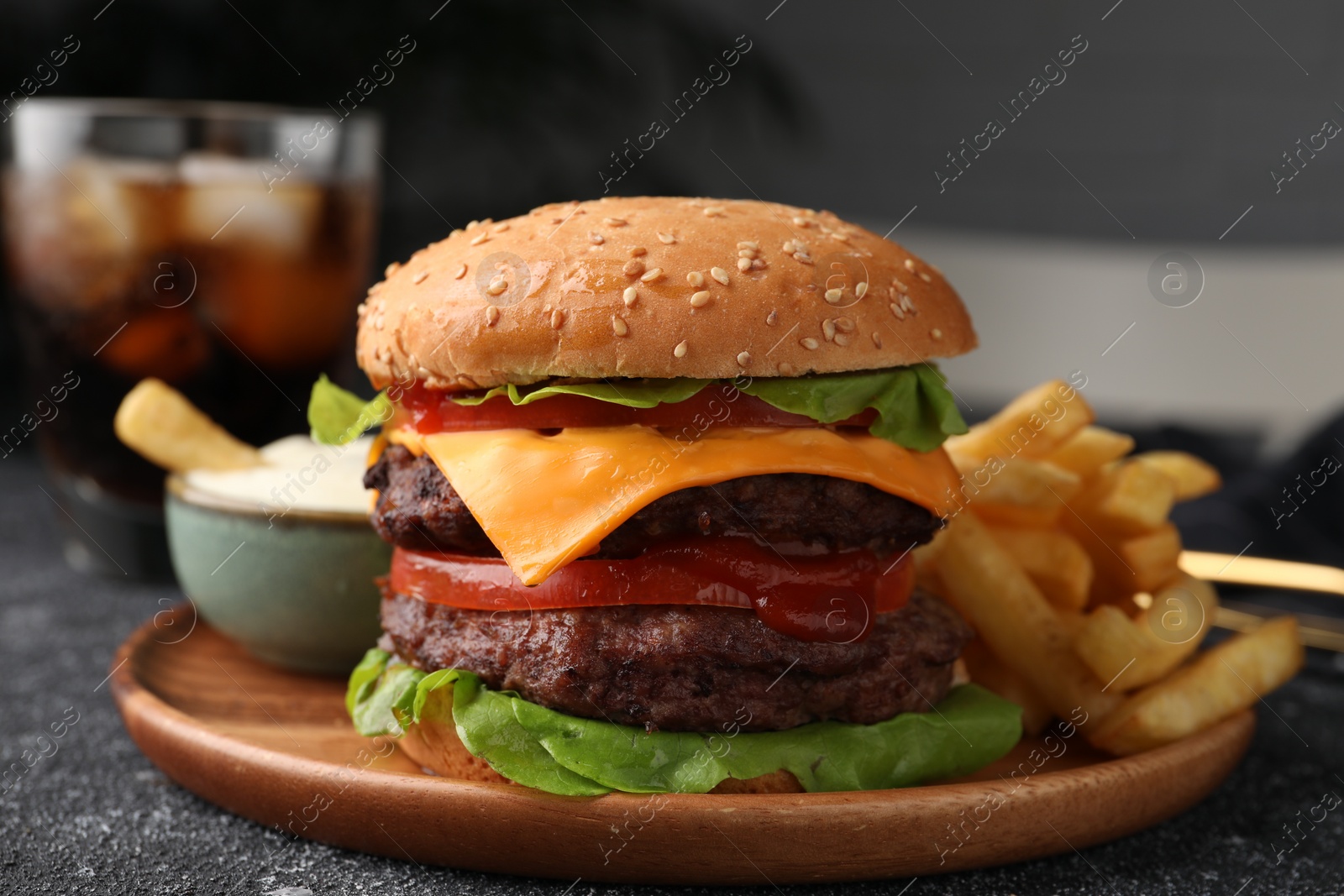 Photo of Tasty cheeseburger with patties, sauce and French fries on grey textured table, closeup