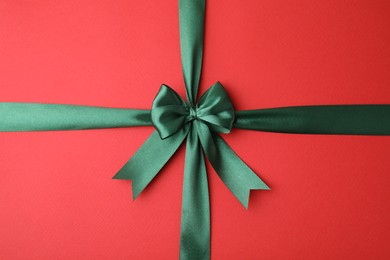 Photo of Green satin ribbon with bow on red background, top view