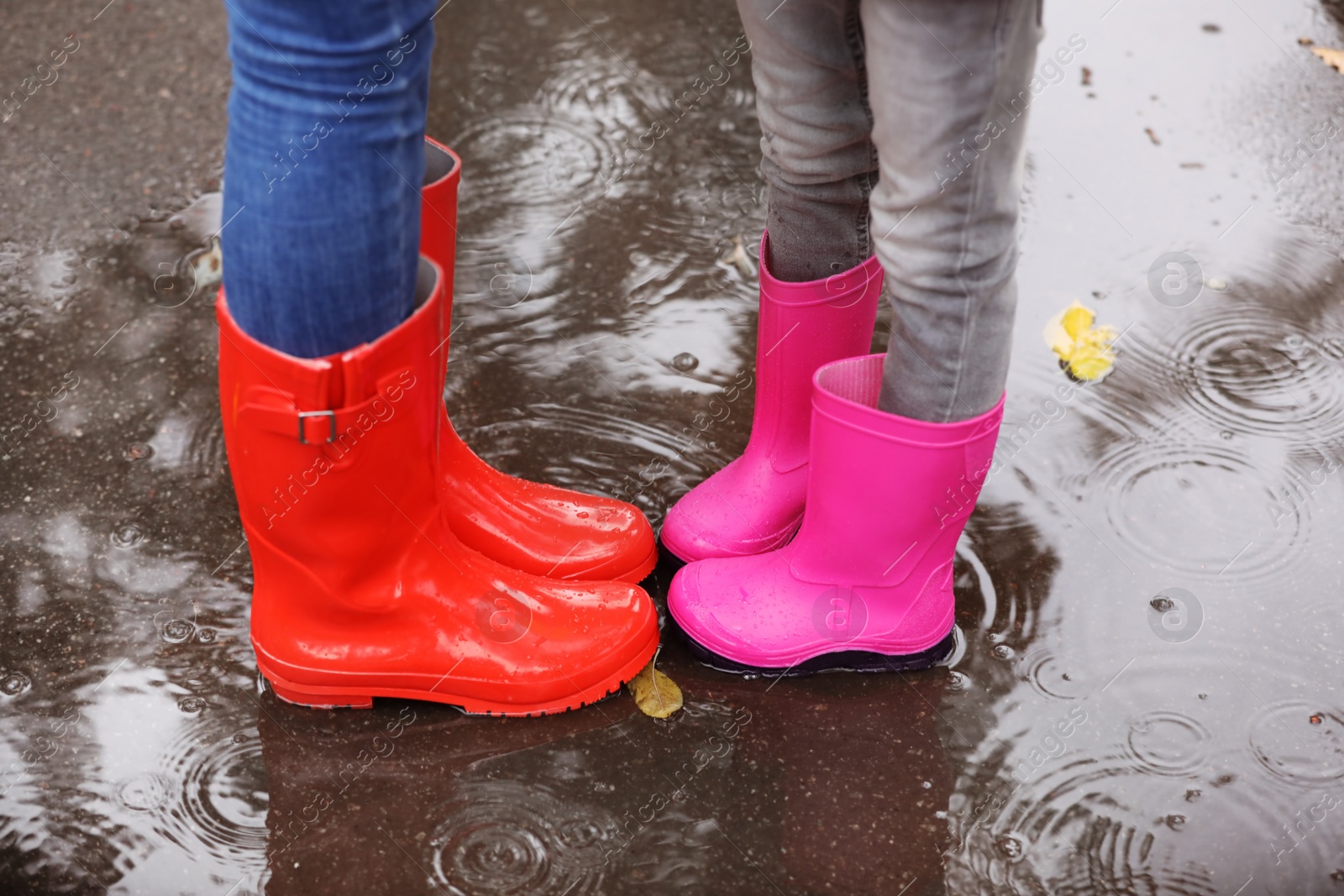 Photo of Mother and daughter wearing rubber boots standing in puddle on rainy day, focus of legs. Autumn walk