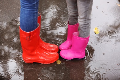 Mother and daughter wearing rubber boots standing in puddle on rainy day, focus of legs. Autumn walk