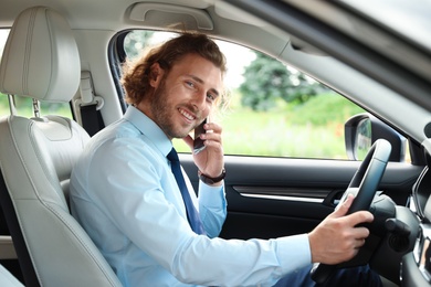 Photo of Attractive young man talking on phone while driving car