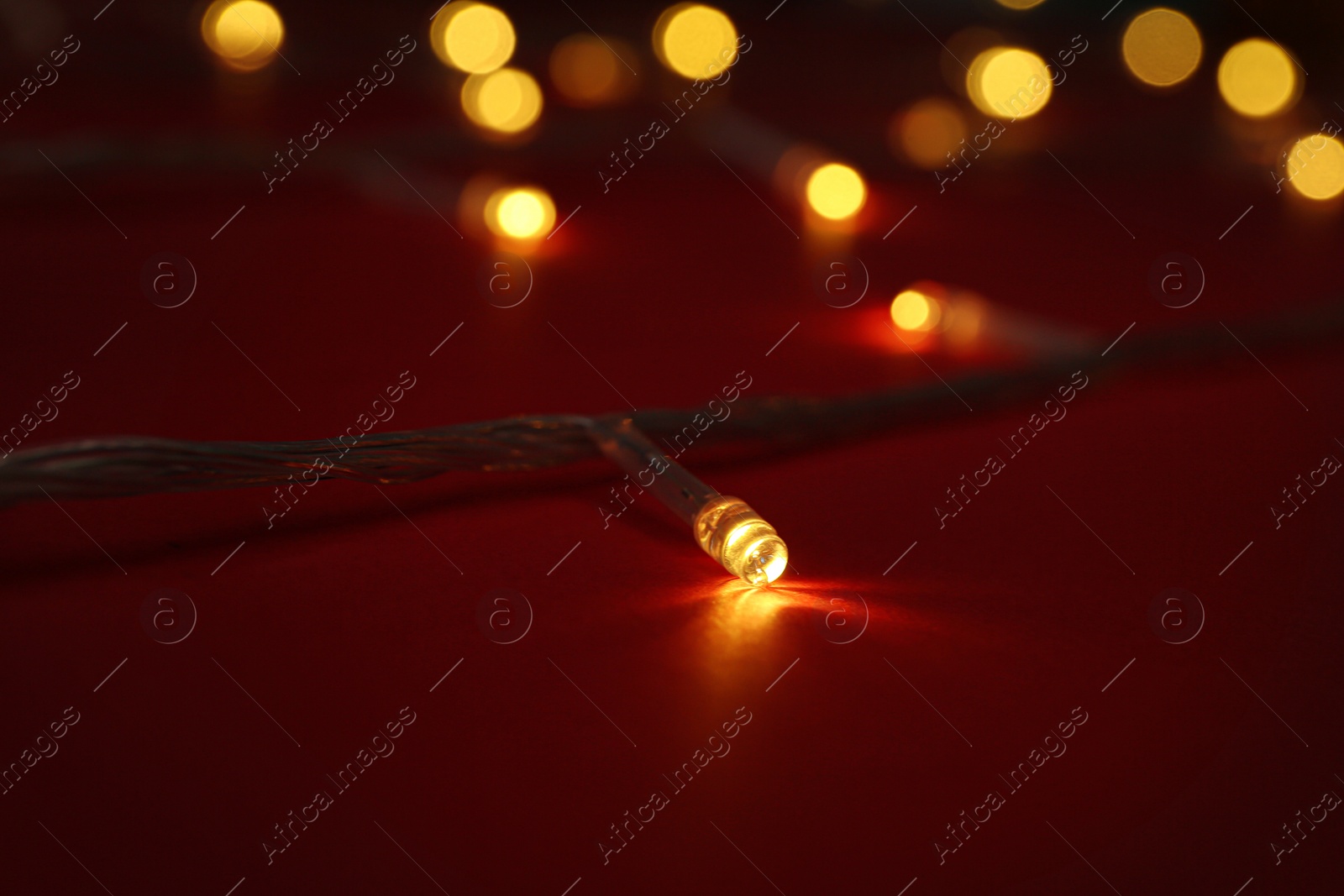 Photo of Glowing Christmas lights on red background, closeup