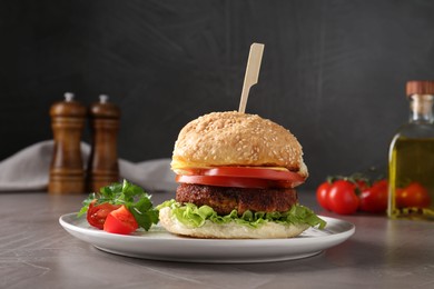 Photo of Plate with delicious vegetarian burger on grey textured table