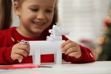 Cute little girl making paper toy for Saint Nicholas day at home, focus on hands