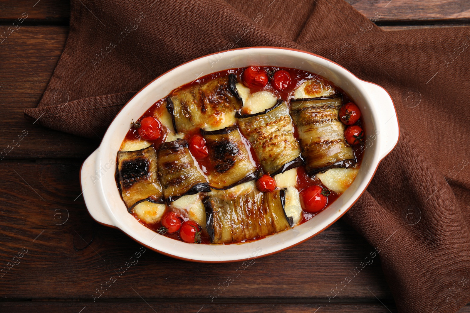 Photo of Tasty eggplant rolls with tomatoes and cheese in baking dish on wooden table, top view