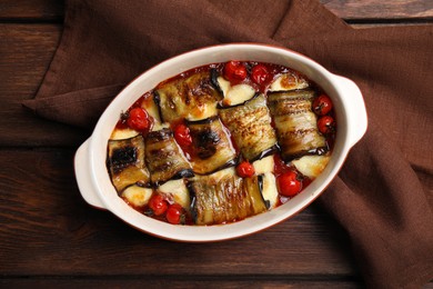 Photo of Tasty eggplant rolls with tomatoes and cheese in baking dish on wooden table, top view