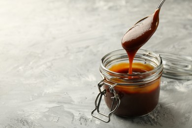 Photo of Taking tasty barbeque sauce from jar with spoon at grey textured table, closeup. Space for text