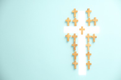 Photo of White cross among small ones on turquoise background, top view with space for text. Religion of Christianity