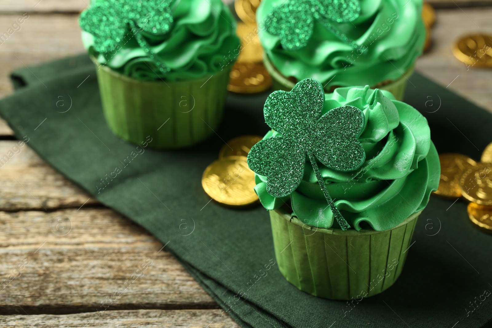 Photo of St. Patrick's day party. Tasty cupcakes with clover leaf toppers and green cream on wooden table, closeup. Space for text