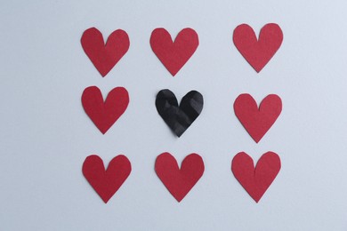 Black crumpled paper heart and red decorative hearts on gray background, flat lay. Relationship problem concept