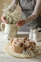 Delicious Italian Easter dove cake (traditional Colomba di Pasqua). Woman putting bouquet on white wooden table