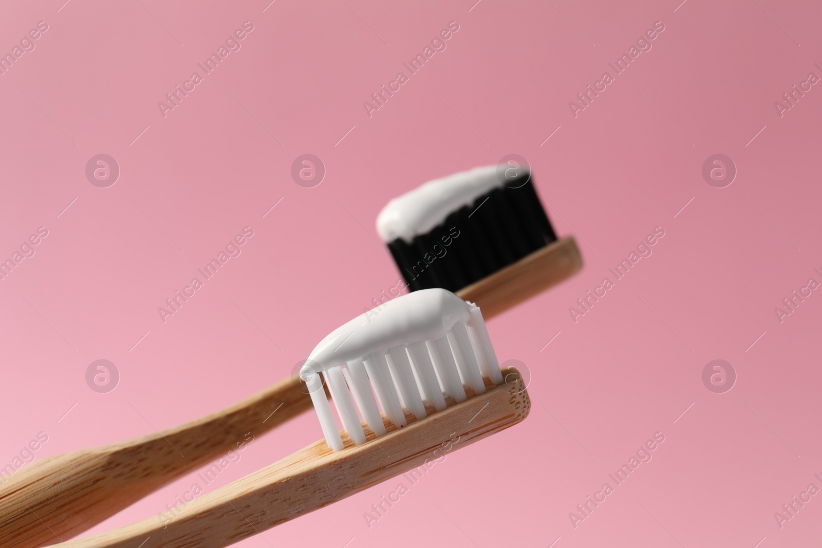 Photo of Wooden brushes with toothpaste on pink background, closeup