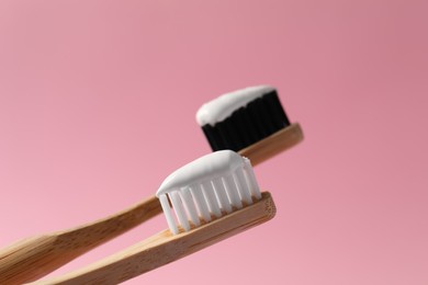 Wooden brushes with toothpaste on pink background, closeup