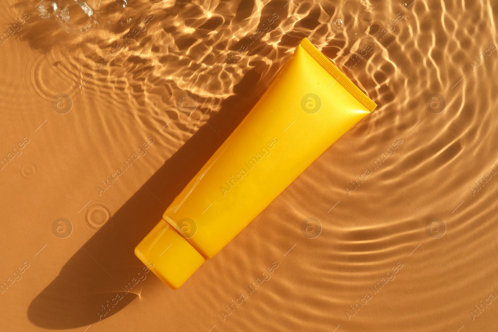 Photo of Tube with moisturizing cream in water on orange background, top view