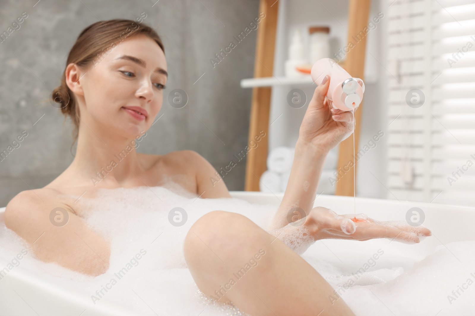 Photo of Woman pouring shower gel onto hand in bath indoors