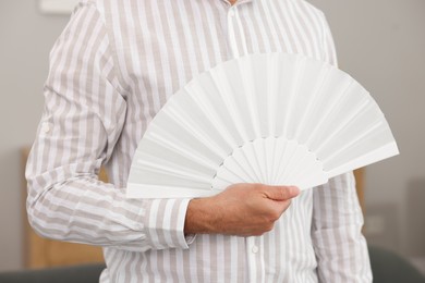 Photo of Man with white hand fan at home, closeup