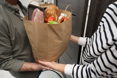 Courier giving paper bag with food products to senior man indoors, closeup