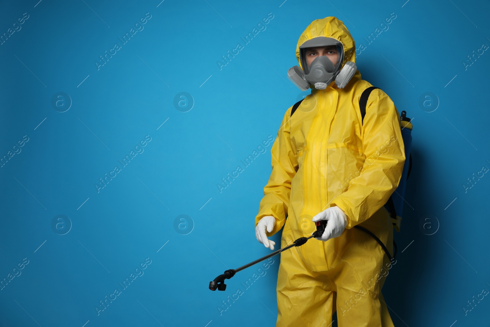 Photo of Man wearing protective suit with insecticide sprayer on blue background, space for text. Pest control