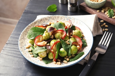 Photo of Plate of delicious salad with Brussels sprouts and roasted apples on wooden table