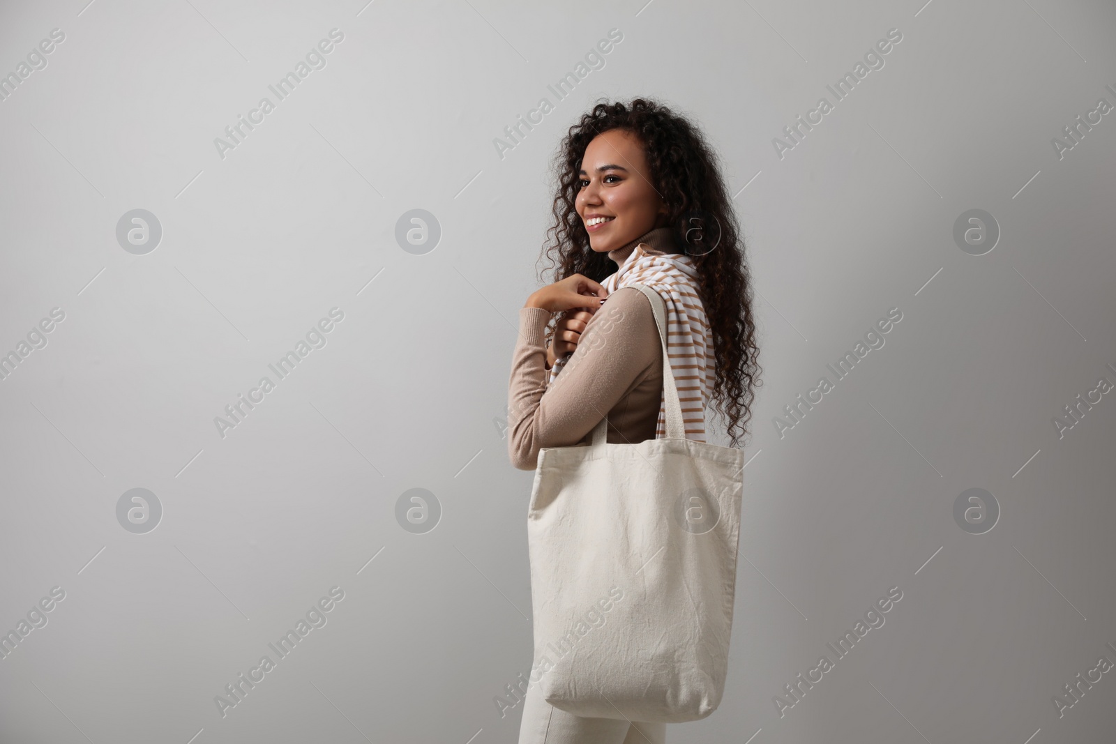 Photo of Happy African-American woman with eco bag on grey background. Space for text