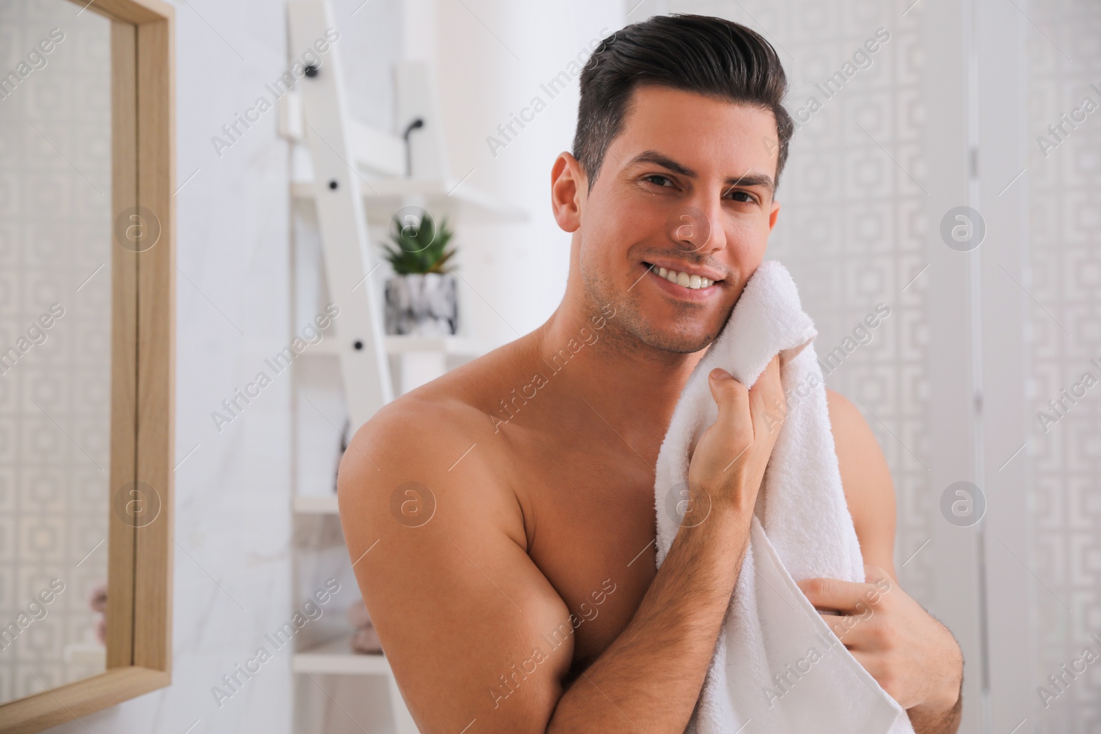 Photo of Handsome man wiping his smooth face with towel  in bathroom after shaving