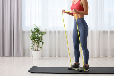 Photo of Woman doing exercise with fitness elastic band on mat at home, closeup. Space for text