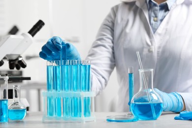 Photo of Scientist dripping liquid from pipette into test tube at white table in laboratory, closeup