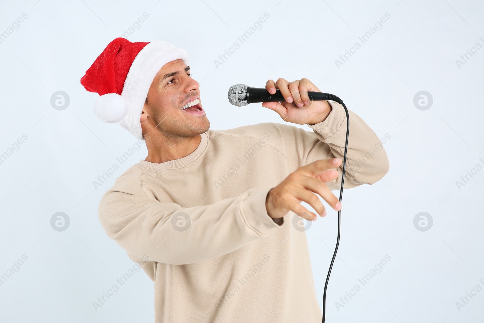 Photo of Emotional man in Santa Claus hat singing with microphone on white background. Christmas music