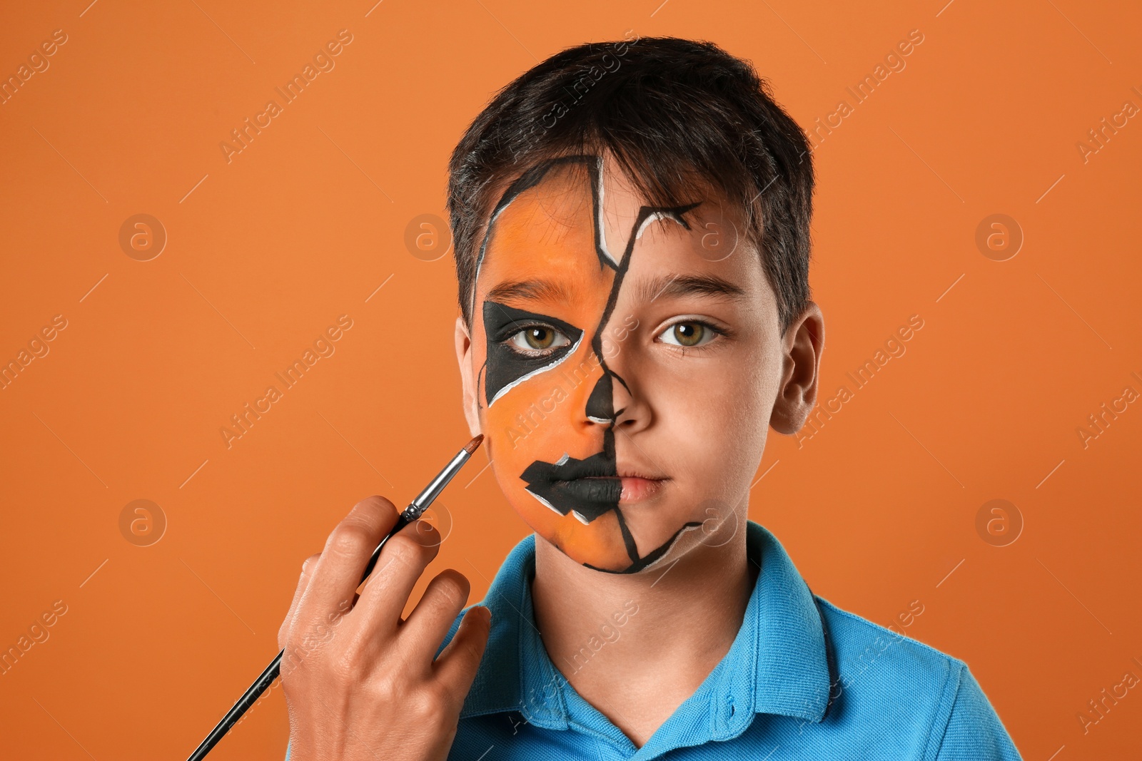 Photo of Artist painting face of little boy on orange background