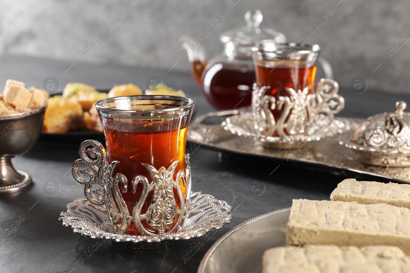 Photo of Turkish tea and sweets served in vintage tea set on black table, closeup