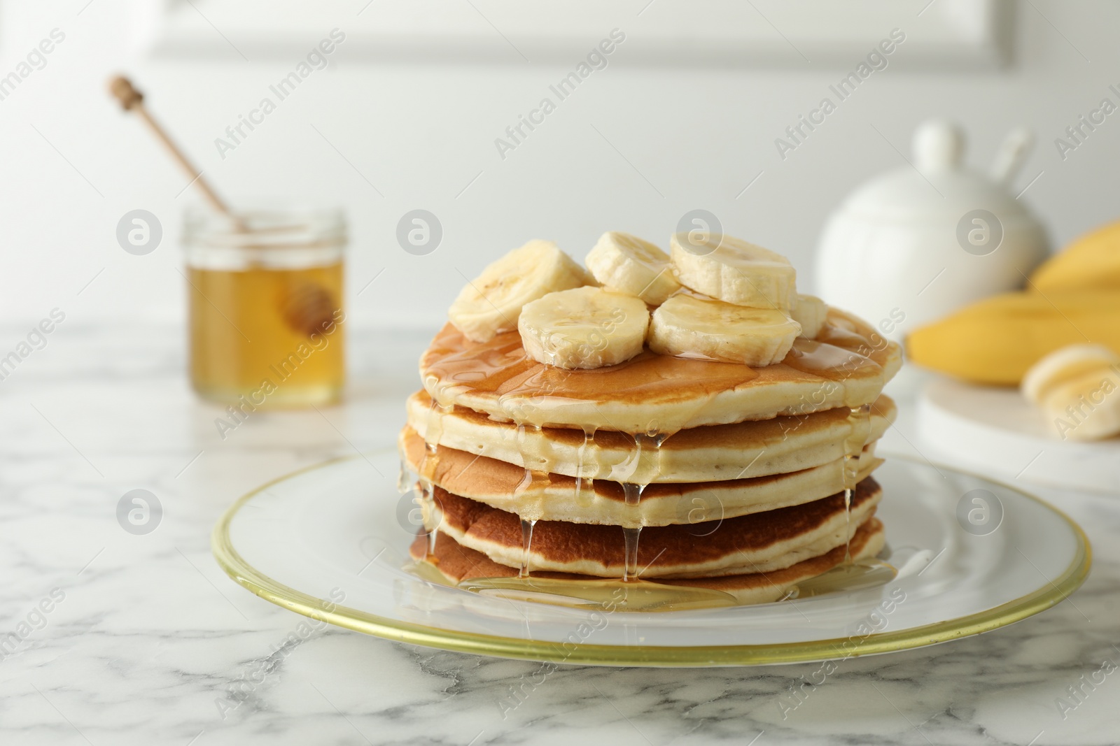 Photo of Delicious pancakes with bananas and honey on white marble table, closeup. Space for text