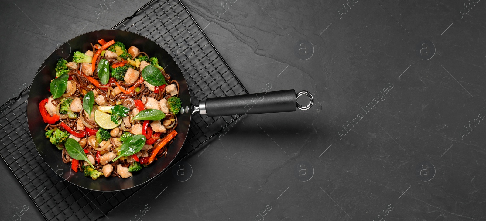 Photo of Stir-fry. Tasty noodles with meat and vegetables in wok on grey textured table, top view. Space for text