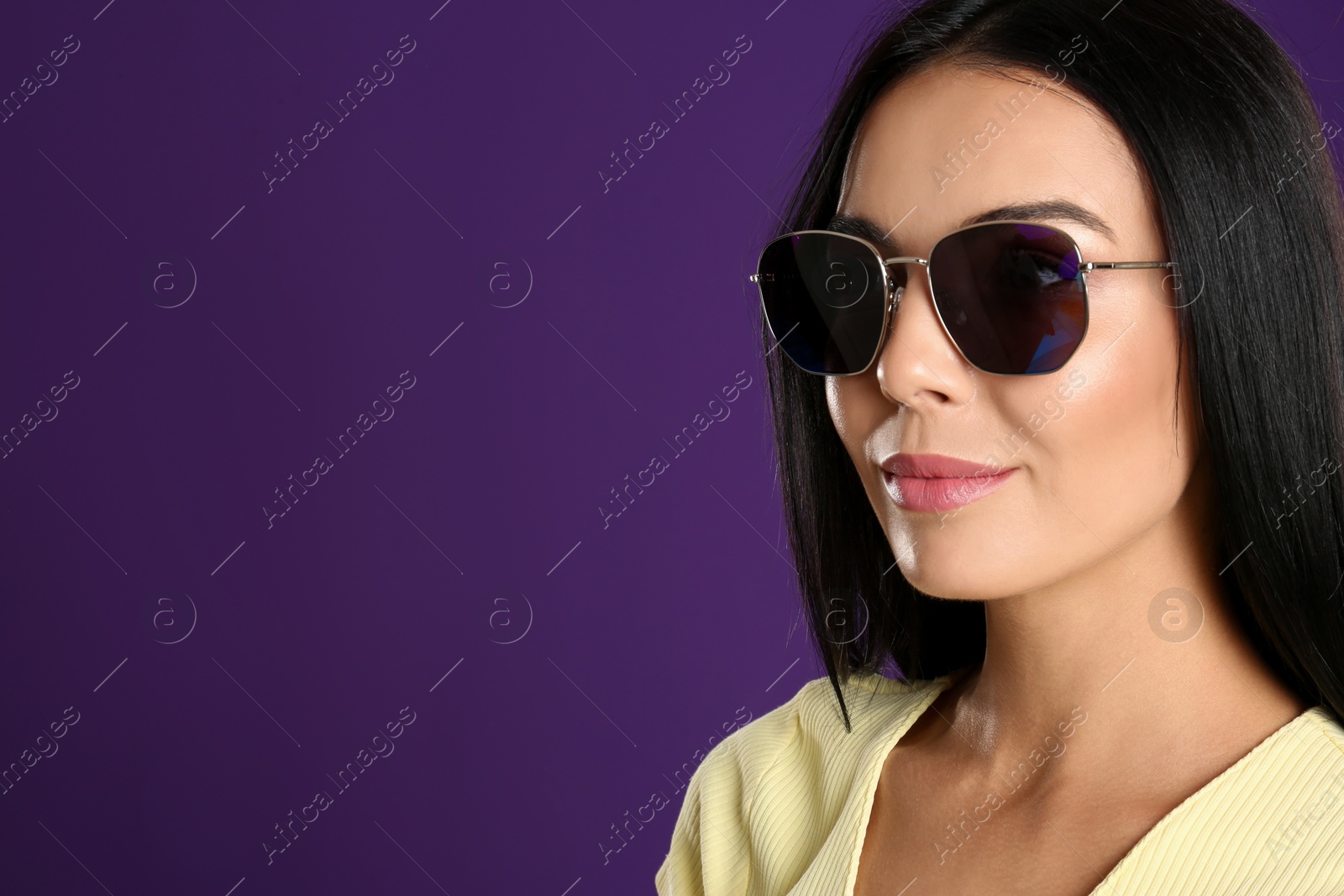 Photo of Beautiful woman wearing sunglasses on purple background, closeup. Space for text