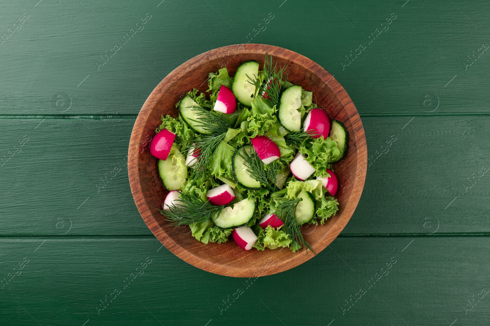 Photo of Delicious salad with radish, lettuce, dill and cucumber on green wooden table, top view