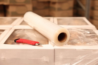 Roll of stretch film and utility knife on wrapped boxes in warehouse