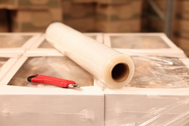 Photo of Roll of stretch film and utility knife on wrapped boxes in warehouse