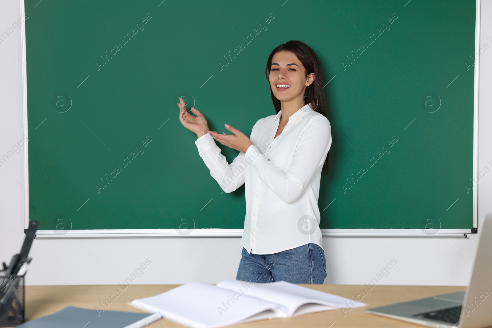 Photo of Happy young teacher giving lesson at blackboard in classroom. Space for text