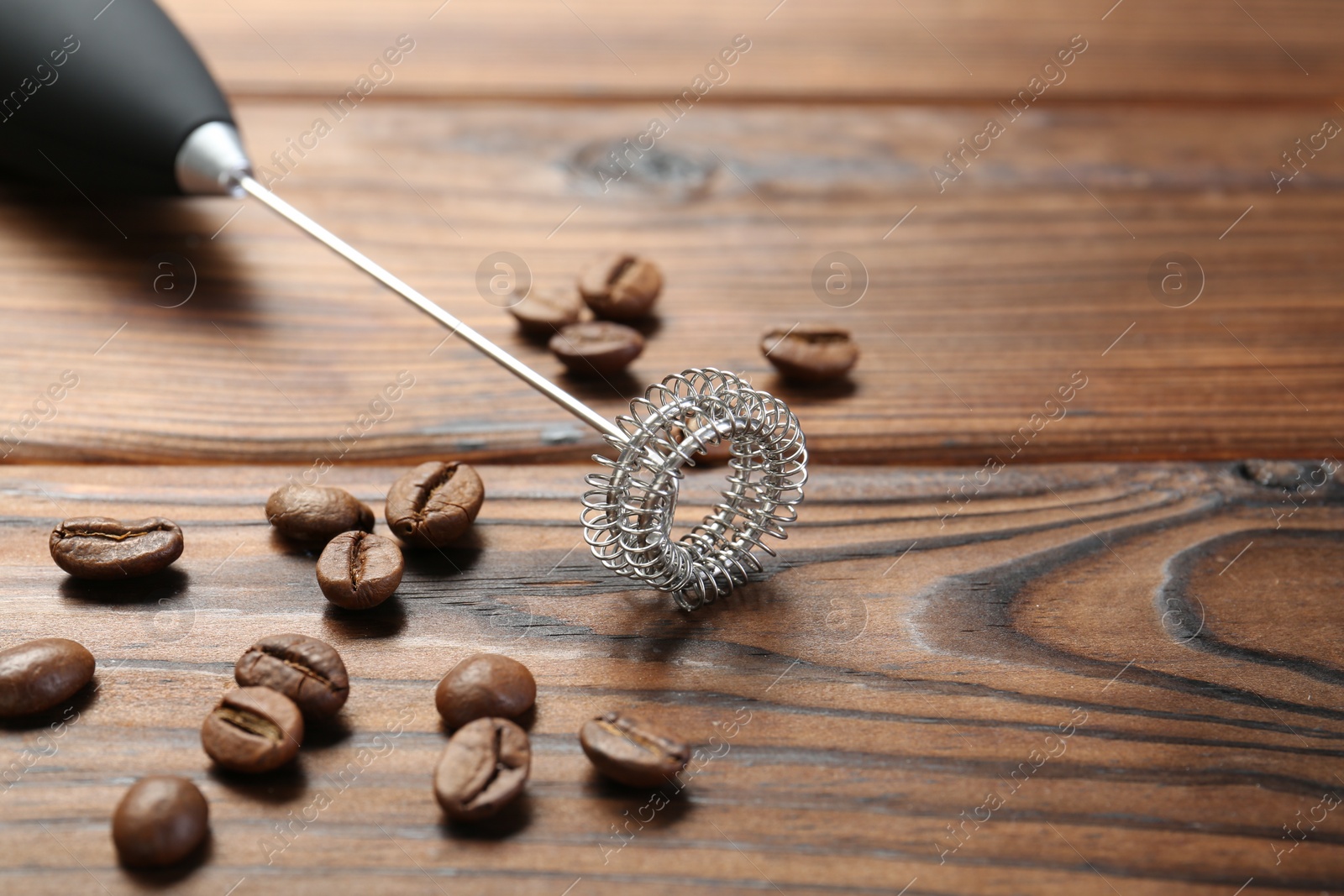 Photo of Black milk frother wand and coffee beans on wooden table, closeup. Space for text