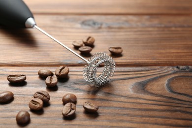 Photo of Black milk frother wand and coffee beans on wooden table, closeup. Space for text