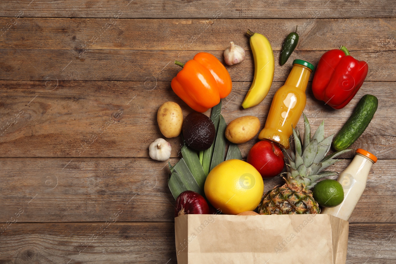 Photo of Shopping paper bag with different groceries on wooden background, flat lay. Space for text